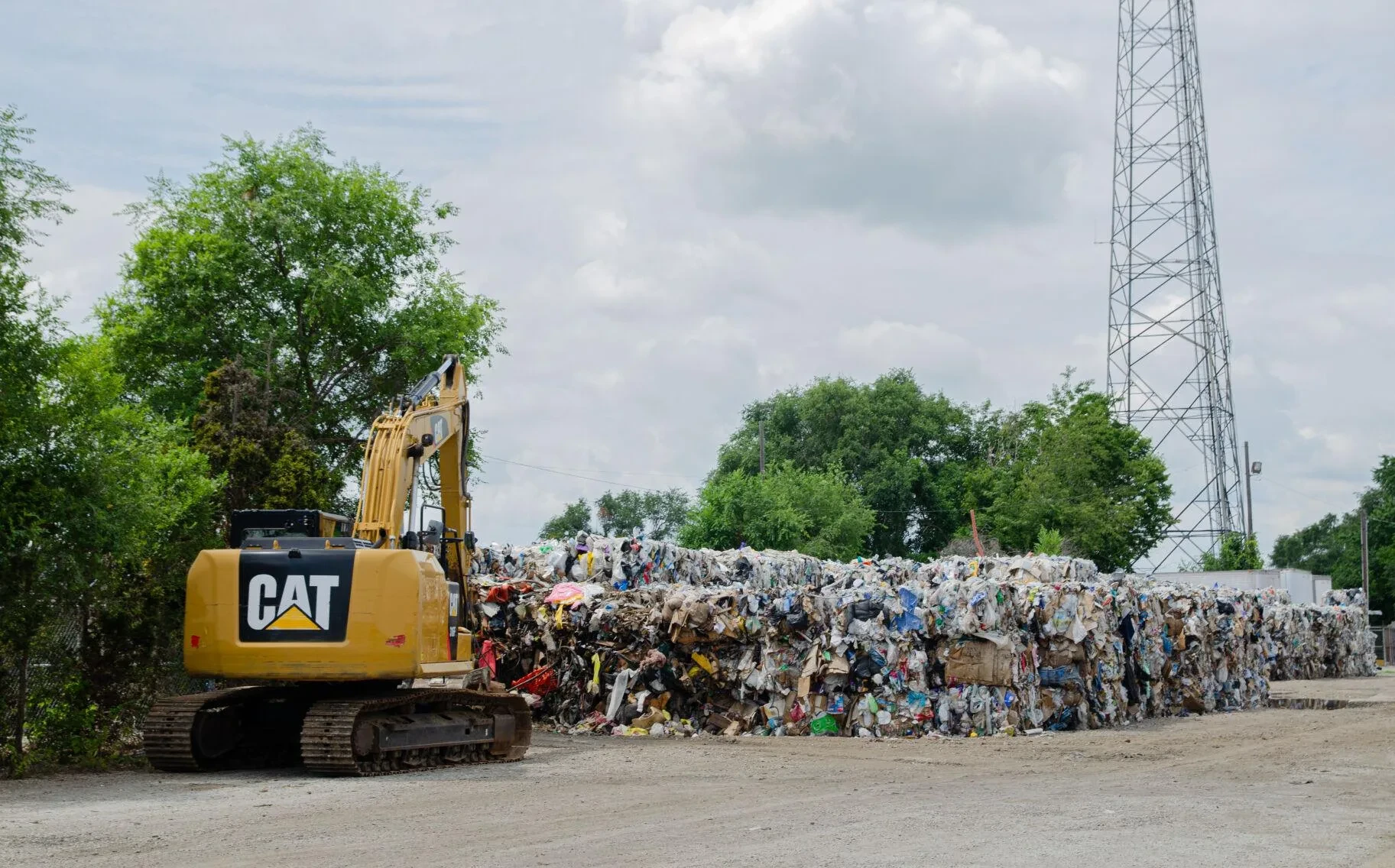 A large yellow crane sits in front of bales of recycling material