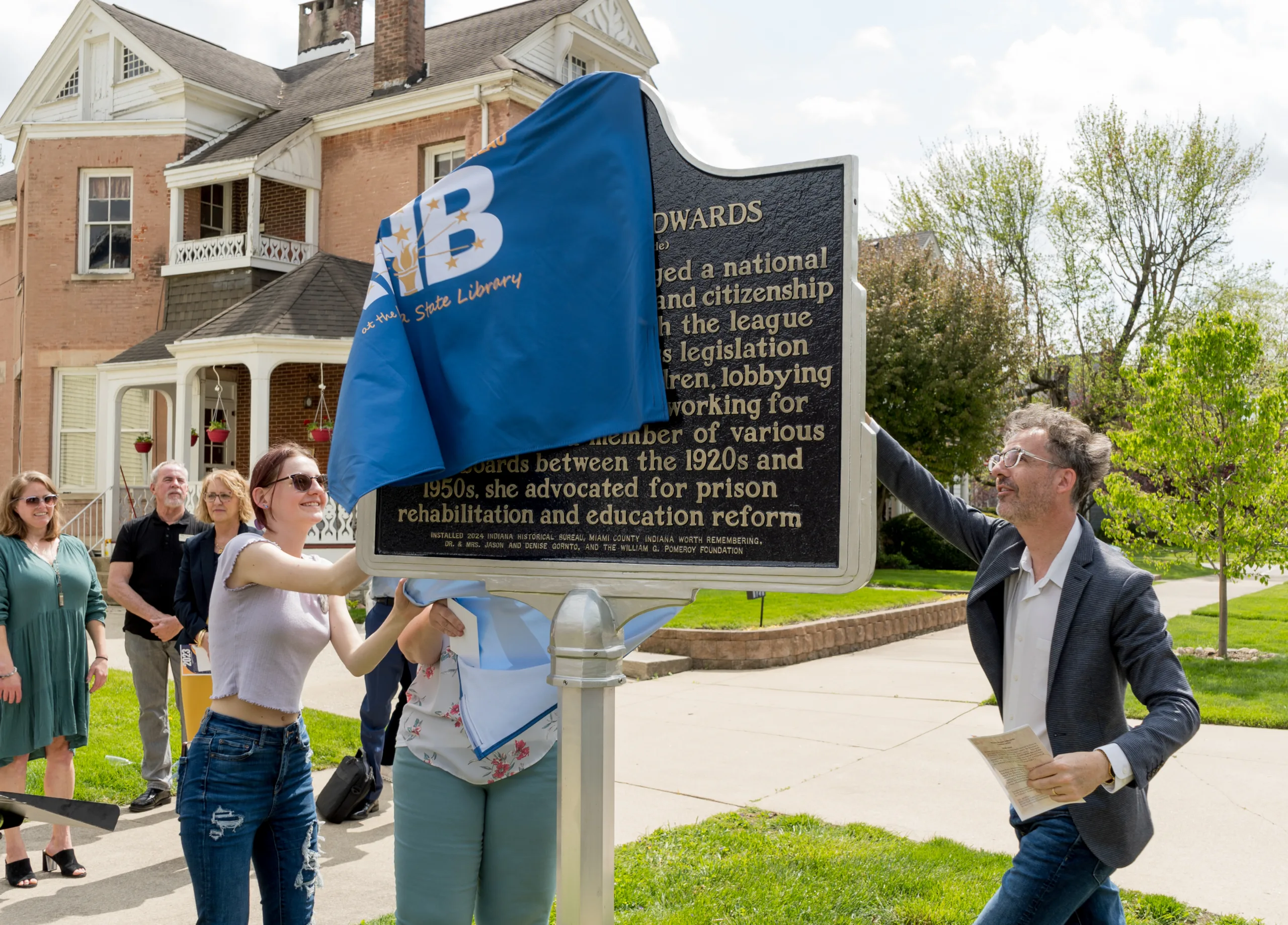 A family removes a blue cover from a historical marker