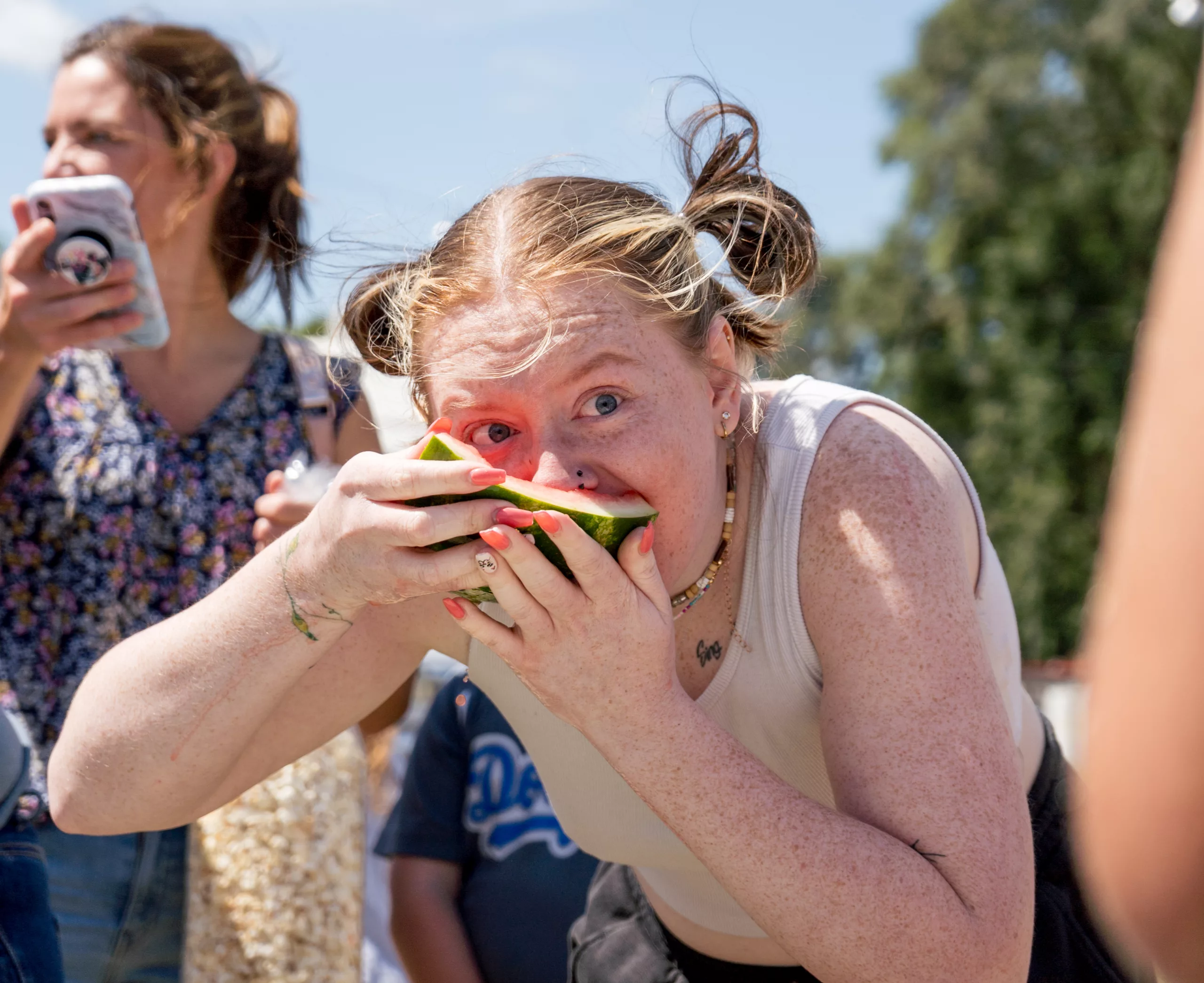 Aria Musselman holds a watermelon close to her face, obscuring the view of her mouth and nose, and peers over the watermelon slice.